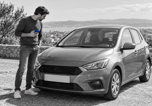 Eine Person prüft ein Auto mit dem Handy in der Hand, Schwarz-Weiß-Foto